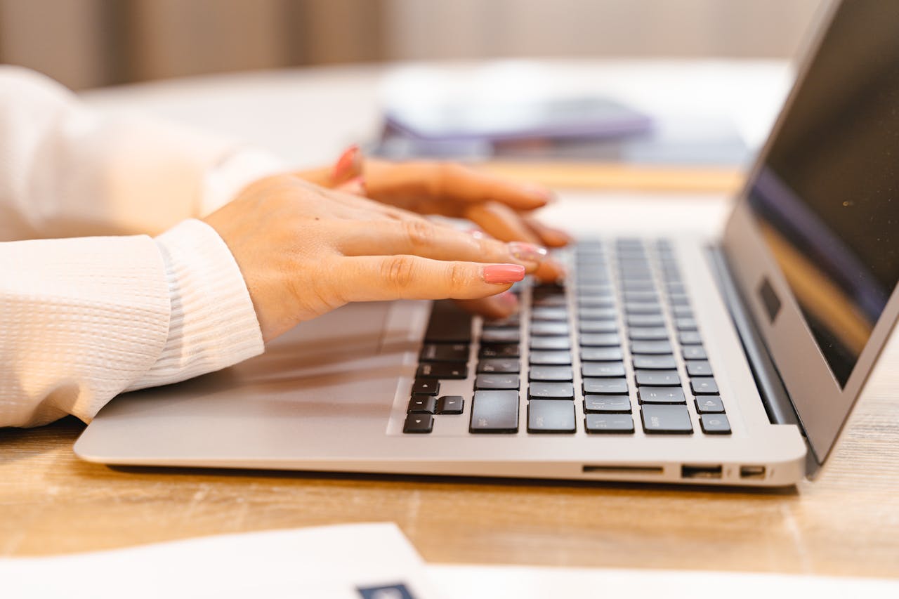 Hands with pink nail polish typing on a laptop keyboard