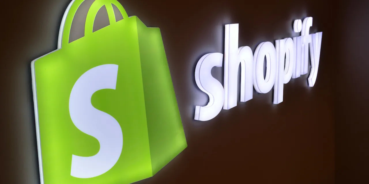 Green shopping bag logo with white 'S' and illuminated word 'shopify' on a dark wall