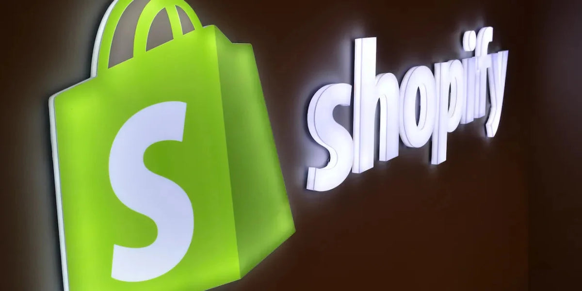 Green shopping bag logo with white 'S' and illuminated word 'shopify' on a dark wall