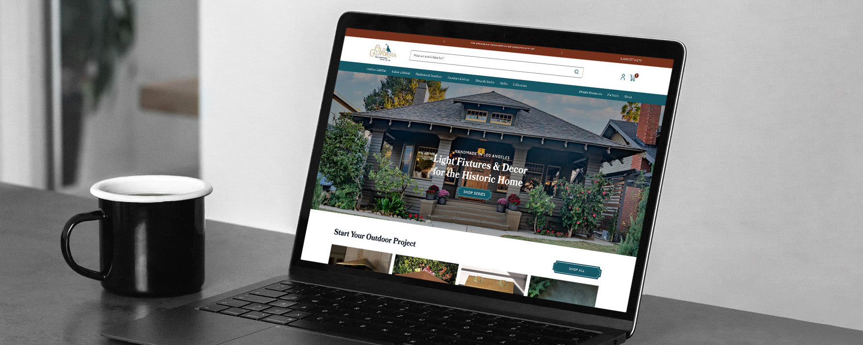 Laptop showing Old California homepage banner 'Light Fixtures & Décor for the Historic Home' with coffee mug beside it