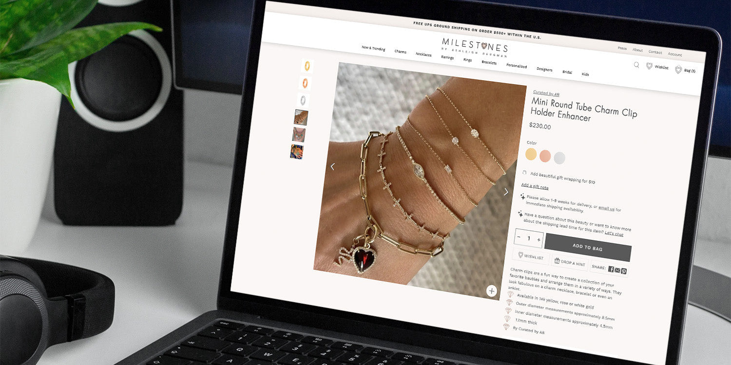 Laptop screen showing MILESTONES product page: Mini Round Tube Charm Clip Holder Enhancer with bracelets; 'ADD TO BAG' button