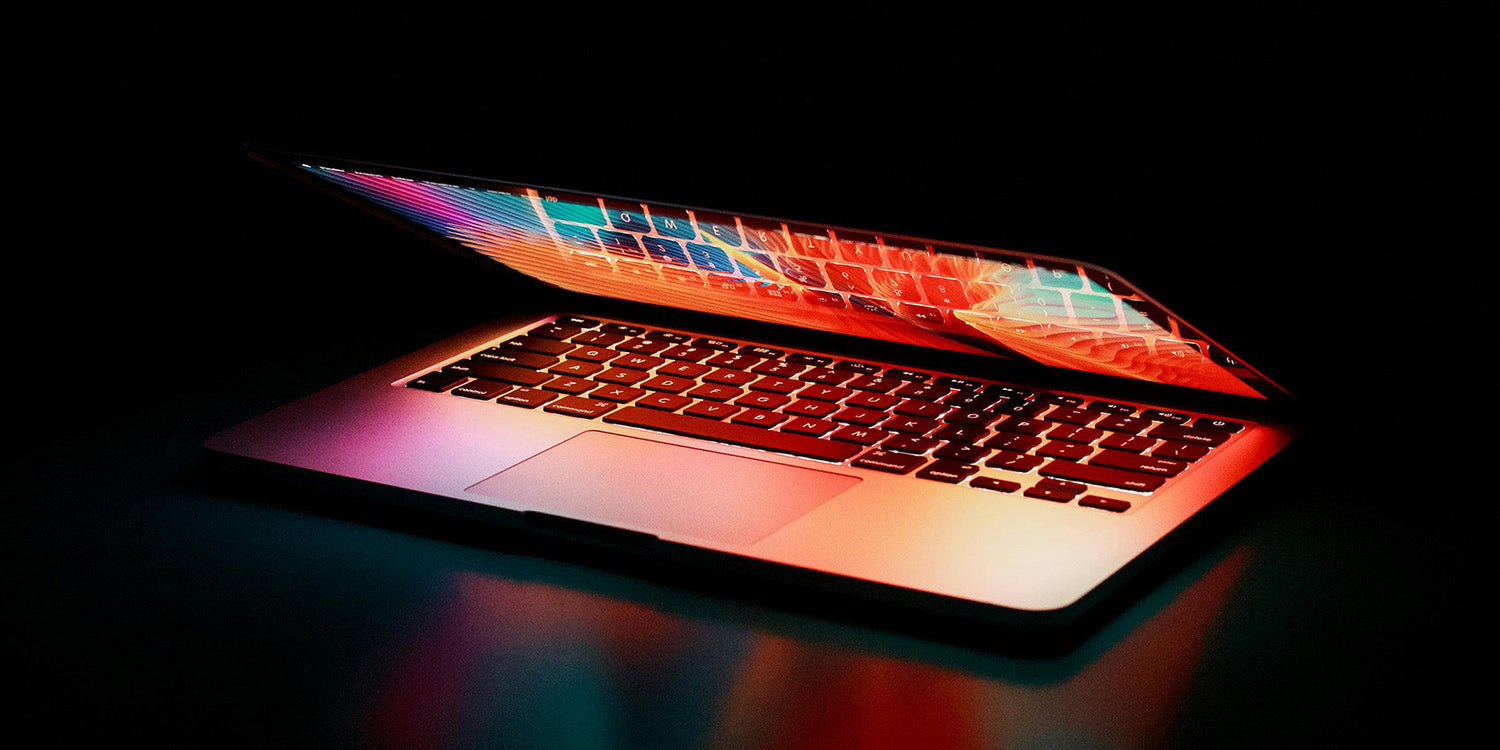 Partially closed laptop showing colorful screen reflections and a backlit keyboard on a dark surface.