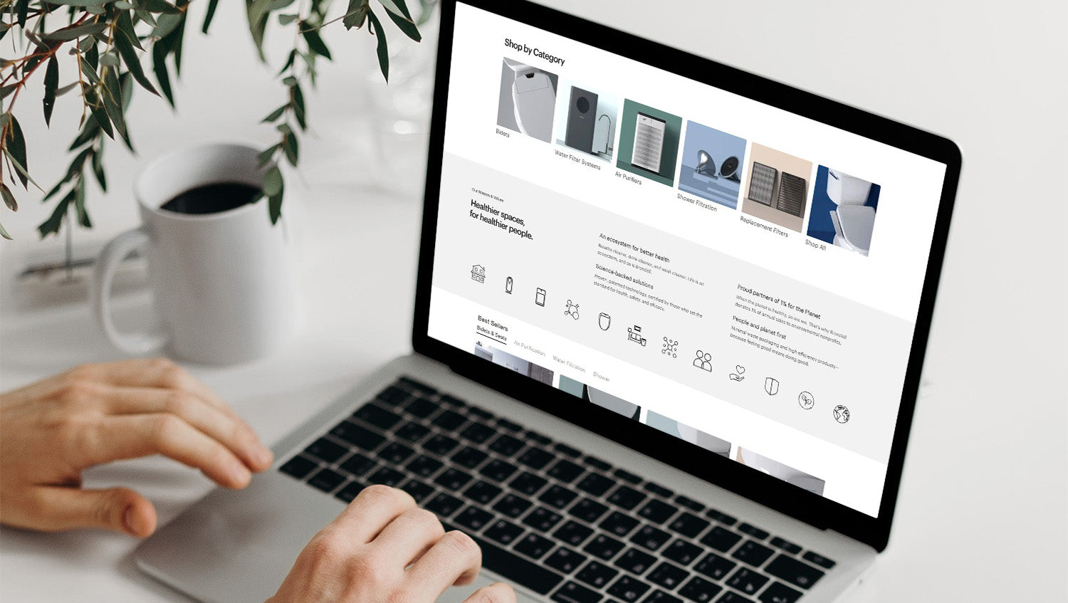 Hands using laptop showing Brondell website with 'Shop by Category' and the text 'Healthier spaces, for healthier people.'